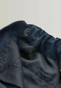 Ceinture en tissu navy avec une texture froncée, dotée d'un bouton transparent et d'un élastique intérieur ajustable pour un fit sécurisé.
