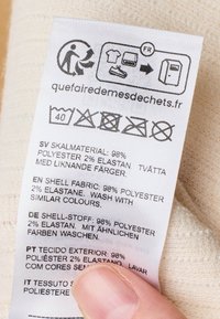 Kledinglabel van stof met verzorgingsinstructies in meerdere talen. Witte achtergrond met zwarte tekst en verzorgingssymbolen.
