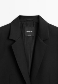 Schwarzes Blazer mit Reverskragen, von oben präsentiert. Innenfutter aus glattem Stoff. Etikett mit "Massimo Dutti" und "Made in Portugal."