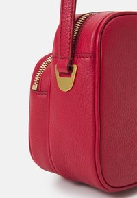 Červená kožená kabelka s texturovaným povrchem, vybavená zlatým zipem a kováním, s kulatým tvarem a krátkým popruhem.