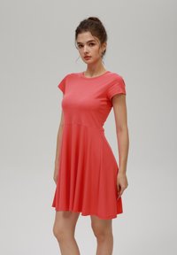 Koralli lyhythihainen mekko, jossa on pyöreä pääntie ja A-linjainen hame. Valmistettu pehmeästä kankaasta, jossa on sileä pinta, ja siinä on fitted bodice.