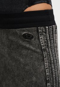 Κοντινό πλάνο μαύρης ελαστικής μέσης και ξεθωριασμένου μαύρου τζιν παντελονιού με κάθετη ραφή και μικρό οβάλ έμπλαστρο στο πλάι.