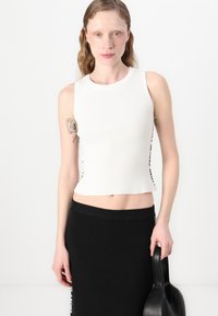 Hvit, ribbestrikket, ermeløs topp med en cropped passform, kombinert med et svart ribbestrikket skjørt. Antrekket har en jevn tekstur og et minimalistisk design.