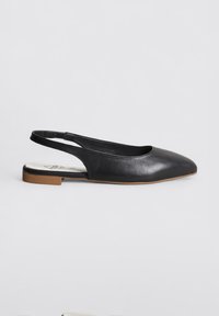 Zapatos planos de cuero negro con talón descubierto y punta afilada, de textura suave y con un pequeño acento de goma marrón en el tacón. Diseño minimalista, sin embellishments.