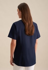 Camicia corta azzurra con vestibilità rilassata, tessuto morbido, scollatura rotonda e spacchi laterali, abbinata a pantaloni bianchi.