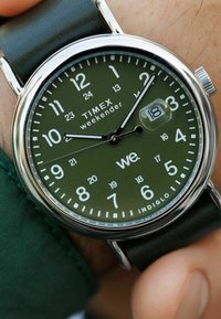 Timex Weekender kellaga, rohelise numbrilaud, must nahkrihm, kuupäevaaken näitab 18, näidiku käed näitavad 10:10:07.