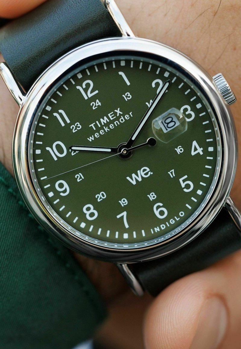 Timex Weekender kellaga, rohelise numbrilaud, must nahkrihm, kuupäevaaken näitab 18, näidiku käed näitavad 10:10:07.