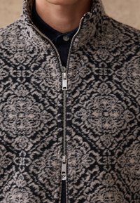 Kootud lukuga jakk, millel on tekstuuriga halli ja mereväe lillemustrit, hõbedase metallist tõmbluku ja kõrge kraega soojuse tagamiseks.