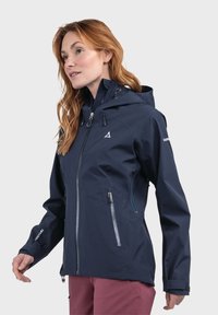 Marineblauer wasserdichter Jacke mit verstellbarem Kapuze, frontalem Reißverschluss, zwei seitlichen Reißverschlusstaschen und Logodetail am Ärmel. Glattes, leichtes Material.