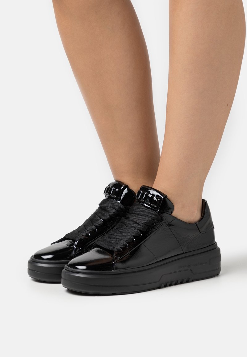 Zwarte gepatineerde leren sneakers met dikke rubberen zolen, getextureerde zwarte veters en gewatteerde enkelaccenten. Strak ontwerp met glanzende afwerking.