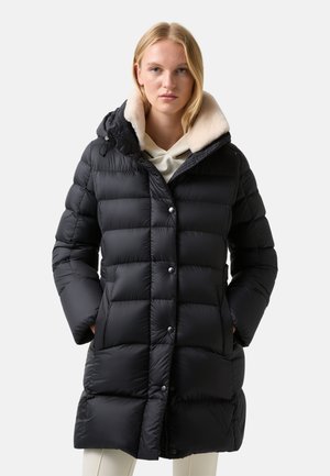 Sort pufferjakke med quiltet design, sølvknapper og en kontrasterende blød creamfarvet krave. Har en hætte og sidelommer.