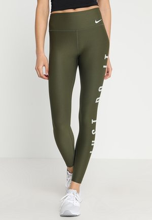 Zielono-oliwkowe legginsy Nike, wysoka talia, z białym napisem "JUST DO IT" po boku, wykonane z gładkiego, elastycznego materiału. Widziane białe buty sportowe.