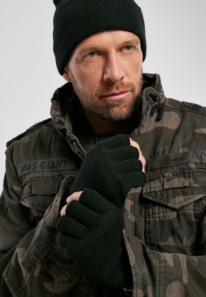Mustad must äärtega mustad sõrmikkindad ja must beanie on kantud rohelise kamoflaažijakiga, millel on lukuga ja mitmed taskud.