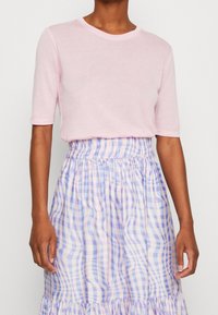 Top rosa chiaro a maniche corte abbinato a una gonna a quadri pastello con tonalità di blu, viola e giallo, vita arricciata e orlo arricciato.