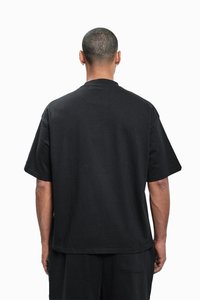 Melns īss piedurkņu T-krekls ar vaļēju piegriezumu, izgatavots no teksturētas auduma, ar taisnu griezumu un minimālistisku dizainu bez redzamiem logotipiem.