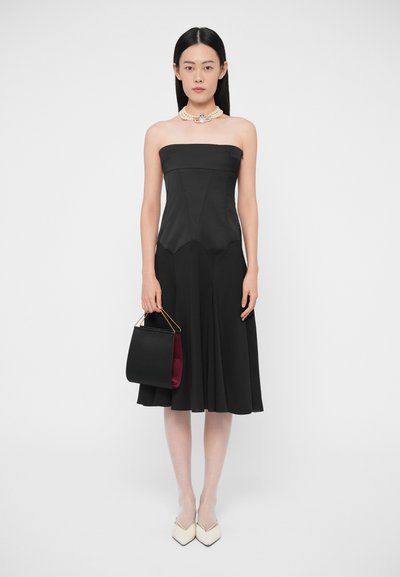 Musta olkaimeton mekko, jossa on istuva yläosa ja levenevä helma. Yhdistetty mustaan ja viininpunaiseen käsilaukkuun sekä kermaan vivahtaviin kärjellisiin korkoihin.