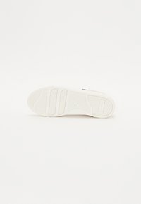 Bílá podešev sneakers s texturovaným gumovým povrchem, vroubkovanými sekcemi pro lepší přilnavost a tkaným vzorem v prostřední části pro flexibilitu.