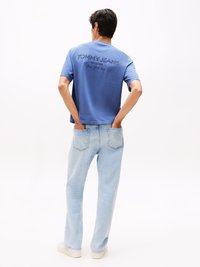 T-shirt di cotone blu con logo sul retro "TOMMY JEANS" in navy, abbinata a jeans di denim azzurri, caratterizzati da un classico design a cinque tasche.