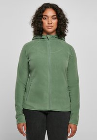 Green fleece jacket with a high collar, zip front, and side pockets. Features a smooth texture and fitted design.