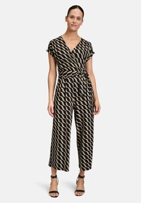 Combinaison portefeuille avec un motif ondulé noir et beige, à manches courtes, taille nouée et pantalons larges. Texture de tissu lisse.