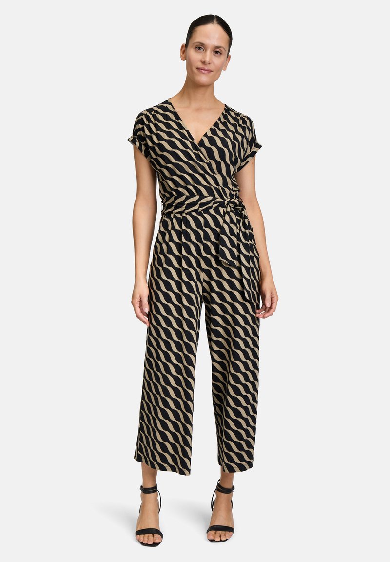 Combinaison portefeuille avec un motif ondulé noir et beige, à manches courtes, taille nouée et pantalons larges. Texture de tissu lisse.