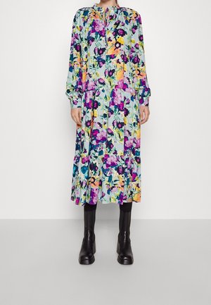 Kwiecista sukienka midi z długimi rękawami, marszczoną talią, dekoltem w kształcie łezki i czarnymi botkami do połowy łydki na jednolitym tle.