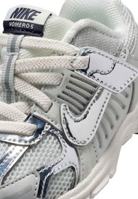 Chaussure Nike Vomero avec tige en mesh gris clair, accents argentés réfléchissants, lacets et sangle à crochet et boucle pour un maintien sécurisé.