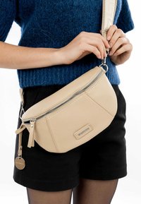Borsa a tracolla in pelle beige con superficie texturizzata, zip diagonale e etichetta con logo. Cinturino regolabile con dettaglio a motivo. Forma compatta e arrotondata.