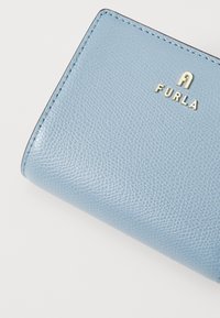 Lyseblå skinnlommebok med teksturert overflate, med et gullprentonsert logo "FURLA" og pent søm langs kantene.