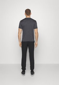 Gray t-shirt with short sleeves, paired with black sweatpants, viewed from the back. Plain design, soft fabric, and relaxed fit.