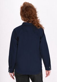 Chemise à manches longues bleu marine avec des poignets à boutons, un col et une texture lisse. La vue arrière montre une coupe droite et des coutures.