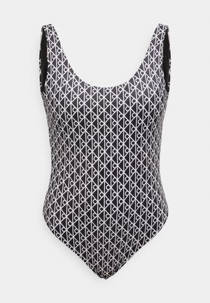 Bañador de una pieza negro con un patrón geométrico blanco de líneas diagonales y lazos, con un escote redondo y tirantes de hombro medianos.