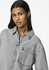 Gray denim button-up shirt with a pocket, featuring a collar and visible stitching details. Soft texture and relaxed fit.