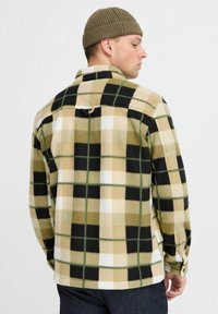 Veste en polaire à motif à carreaux large, présentant des tons de beige, vert et noir. Comprend une fermeture à pression et un col côtelé, texture douce.