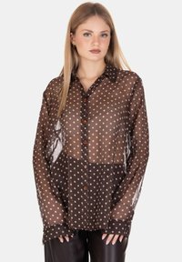 Camicia trasparente marrone con pois bianchi, apertura frontale con bottoni e collo a camicia. Maniche lunghe con polsini abbottonati. Tessuto liscio.