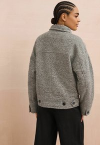 Gray wool blend jacket with a relaxed fit, large collar, long sleeves, and button accents at the hem. Smooth texture and simple design.