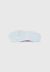 Semelle en caoutchouc blanche d'une sneakers Nike avec des motifs de semelle circulaires et linéaires, affichée sur un fond blanc uni.