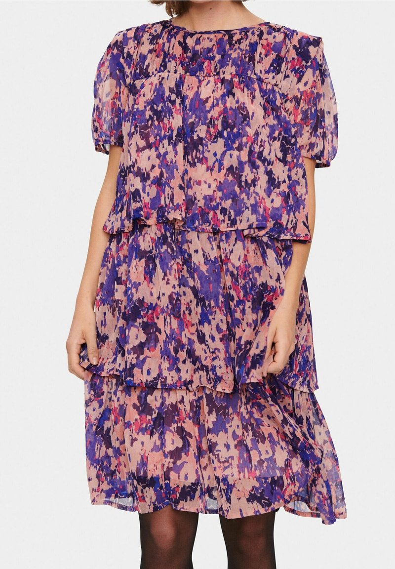 Vestito a stampa floreale viola e rosa con balze sovrapposte, maniche corte a sbuffo e scollatura rotonda; realizzato in tessuto leggero e trasparente.