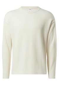 Kremowy, prążkowany sweter z długim rękawem, okrągłym dekoltem, luźnym krojem oraz widoczną metką Reebok wewnątrz dekoltu.