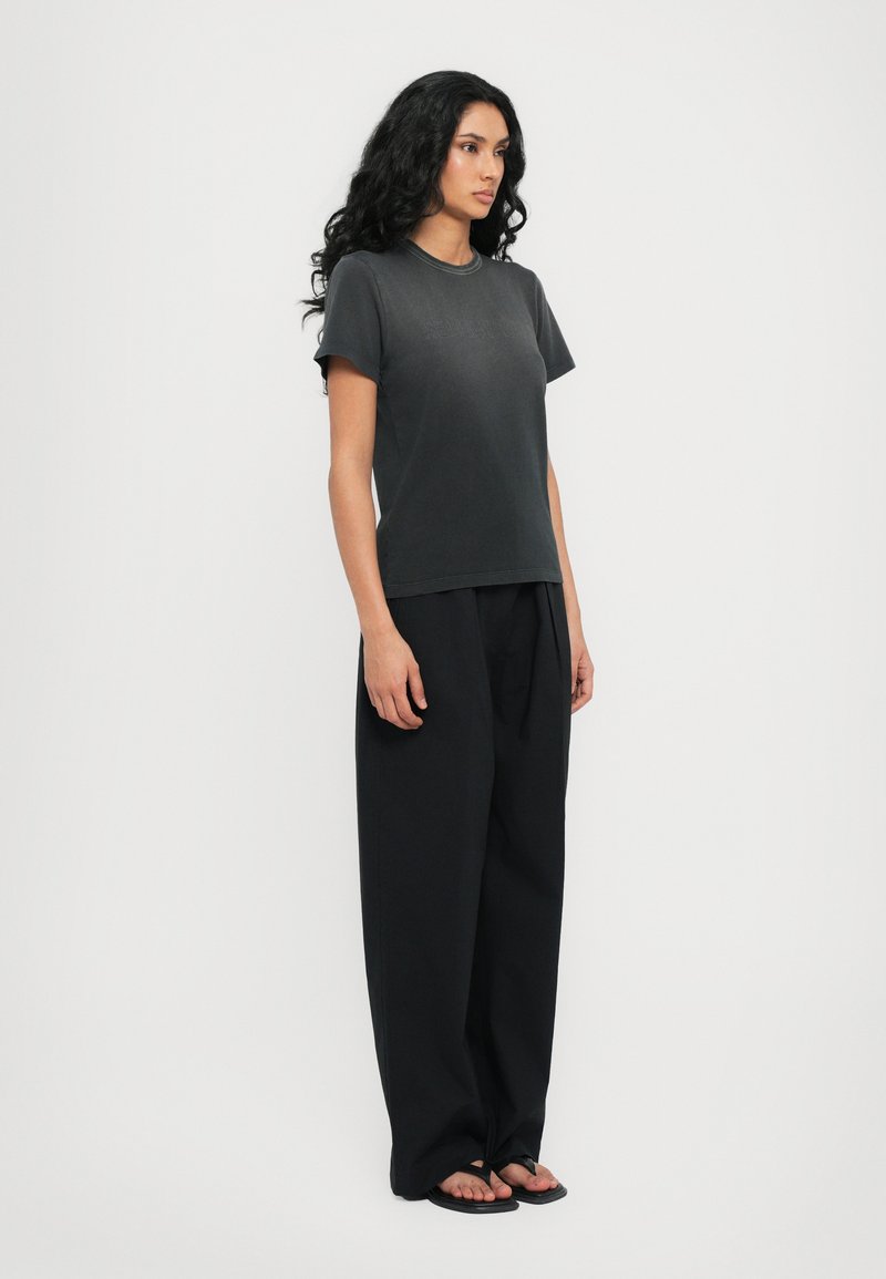 Schwarzes Baumwoll-T-Shirt mit kurzen Ärmeln, kombiniert mit locker sitzenden schwarzen Hosen. Glatte Textur, schlichtes Design und ohne Muster.