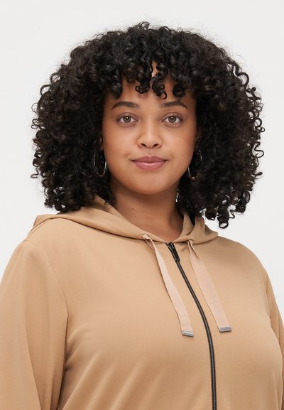 Sweatshirt à capuche beige avec une texture lisse, fermeture éclair devant et cordons de serrage contrastants. Il présente une coupe décontractée et un design simple.
