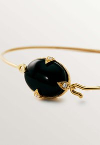 Brazalete de oro con una gran piedra ovalada negra, acentuado con cuatro puntos de oro y pequeños diamantes, superficie lisa y diseño elegante.