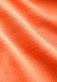 Nahaufnahme eines orangefarbenen, strukturierten Stoffes mit kleinen Perforationen und sichtbarem Strickmuster in sanften Falten.