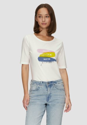 T-shirt blanc à manches courtes avec des graphismes en coups de pinceau multicolores et du texte. Associé à un jean en denim bleu clair.