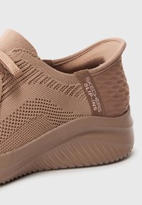 Bruine Skechers instapschoen met een textuur gebreide bovenkant, een gladde hiel en een zachte rubberen zool. Heeft een logo op de hiel.