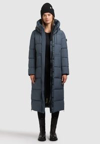 Lang, luftig, blå frakke med hætte, der har lynlås og knaplukning, kombineret med en sort hue og sorte støvler. Glat, isoleret tekstur.