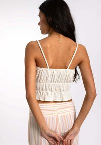 Top cortado blanco con tejido texturizado, tirantes delgados y detalles fruncidos. Combinado con pantalones de colores pastel con rayas verticales.