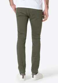 Olive green slim-fit pants, cotton blend, ribbed texture, rear pockets, paired with white sneakers featuring grey accents.