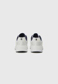Zapatillas deportivas blancas con acentos en azul marino. El diseño presenta una parte superior texturizada, un cuello acolchado y una suela de goma plana. Logo visible en el talón.