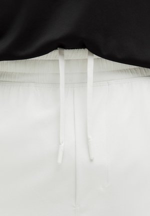 Bele trenirke z elastiko in belimi vrvicami, v kombinaciji z črnim vrhom. Gladka tekstura, športen dizajn.